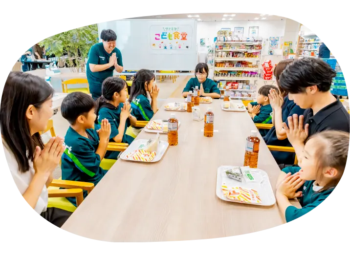 大きなテーブルを囲んで食事をする子どもたちと保護者。ファミリーマートスタッフも見守ります。